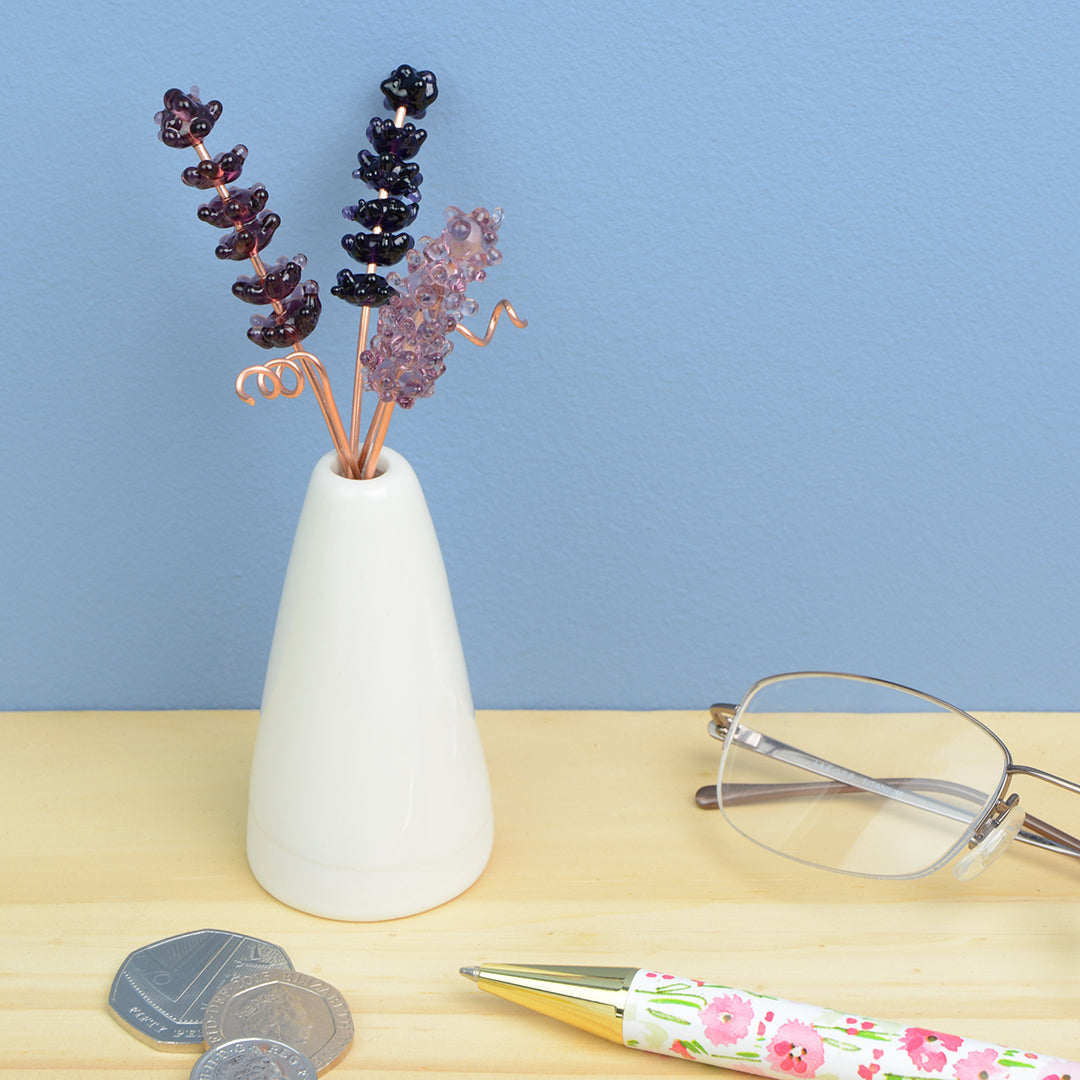 Miniature white porcelain cone vase containing three purple glass lavender stems