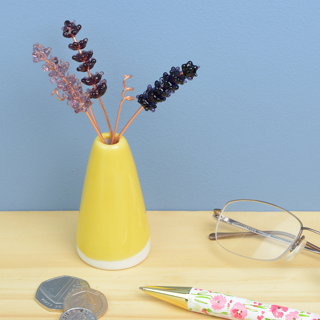 Miniature yellow porcelain cone vase containing three purple glass lavender stems