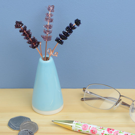 Miniature blue porcelain cone vase containing three purple glass lavender stems
