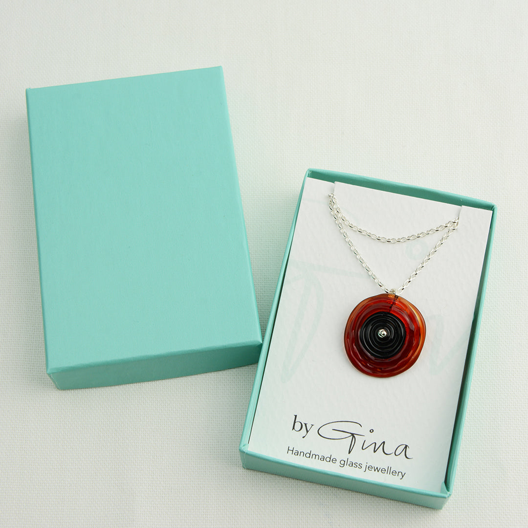 Spiral of red and black glass to replicate a poppy flower on a silver chain in a turquoise gift box