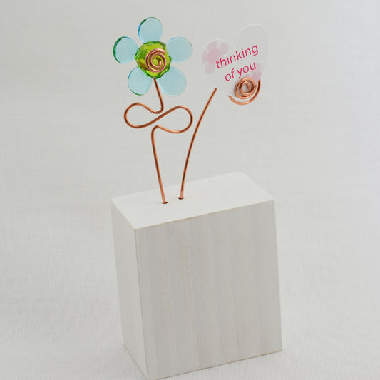 Turquoise and green glass flower on a white wooden block with a paper heart with the message 'Thinking of You'