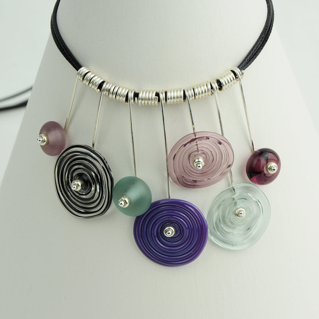 Four spiral beads and three spacer beads in shades of purple and grey on silver headpin drops with silver spiral spacers on black necklace cord