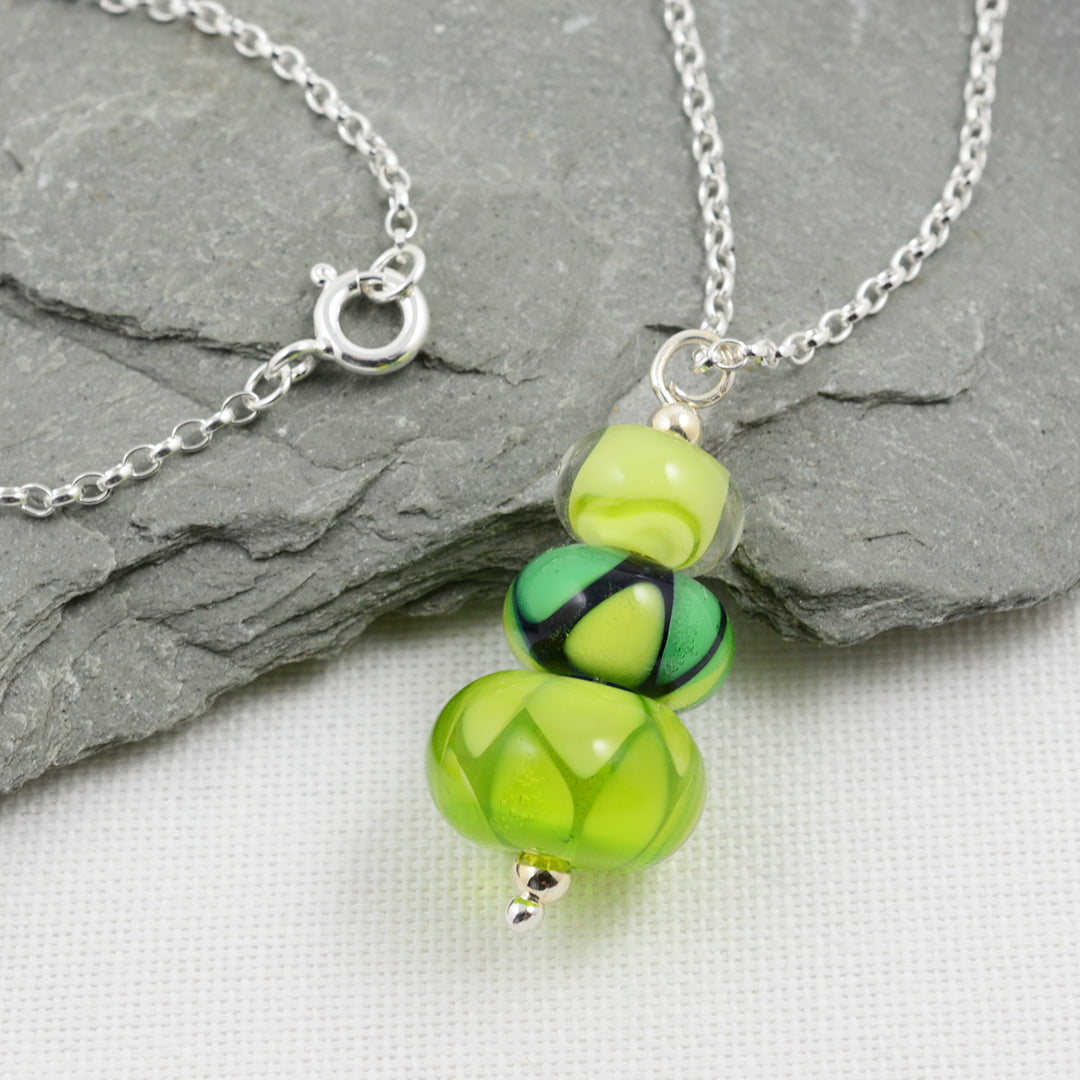 Two green glass beads and one green and blue bead making a pendant on silver chain