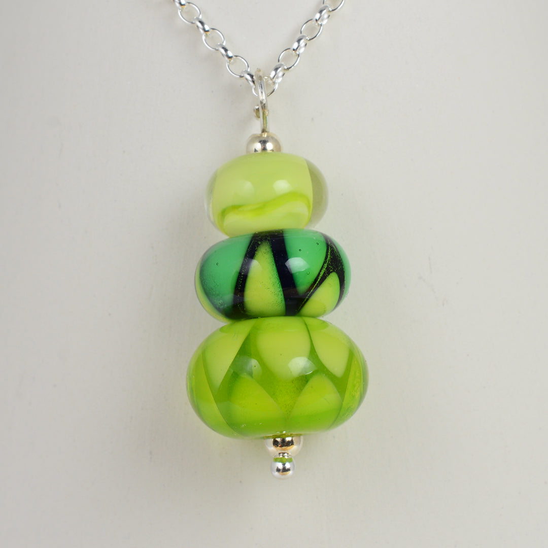 Two green glass beads and one green and blue bead making a pendant on silver chain