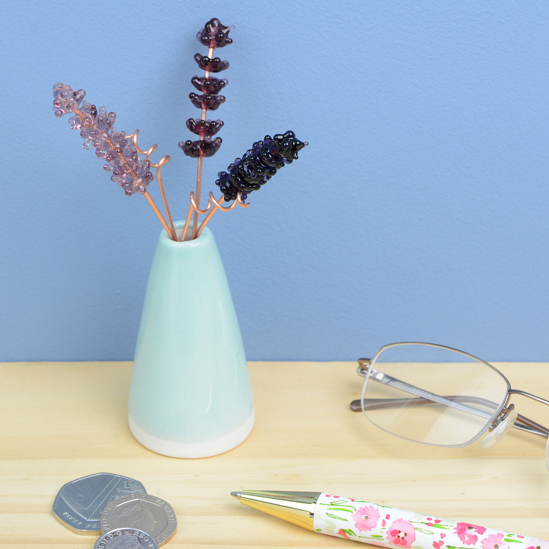 Miniature pale teal porcelain cone vase containing three purple glass lavender stems