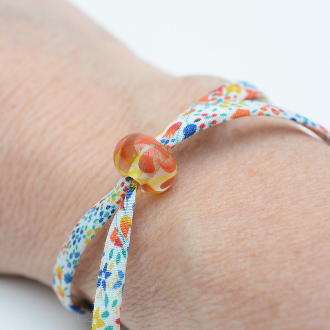 Bracelet made from red, yellow and blue liberty cord with single yellow and orange bead shown being worn on a wrist