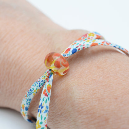 Bracelet made from red, yellow and blue liberty cord with single yellow and orange bead shown being worn on a wrist
