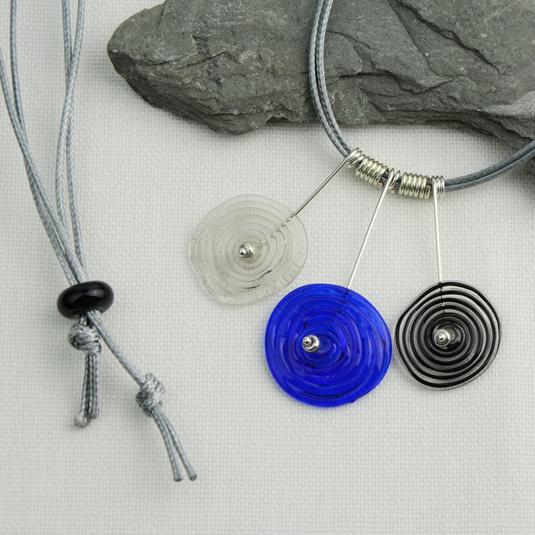 Three spiral beads in grey, blue and black inline on silver headpin drops with silver spiral spacers on grey necklace cord