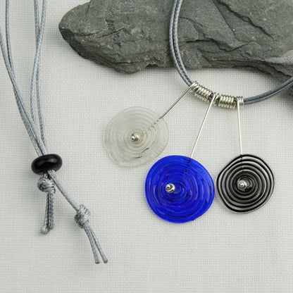 Three spiral beads in grey, blue and black inline on silver headpin drops with silver spiral spacers on grey necklace cord