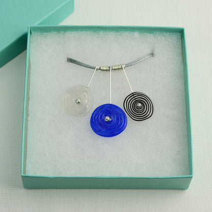 Three spiral beads in grey, blue and black inline on silver headpin drops with silver spiral spacers on grey necklace cord in turquoise gift box
