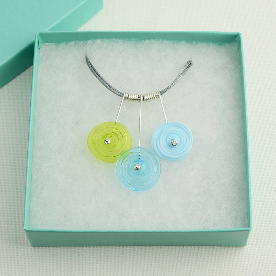 Three spiral beads in lime green, turquoise and pale blueon silver headpin drops with silver spiral spacers on grey necklace cord in tirquoise gift box