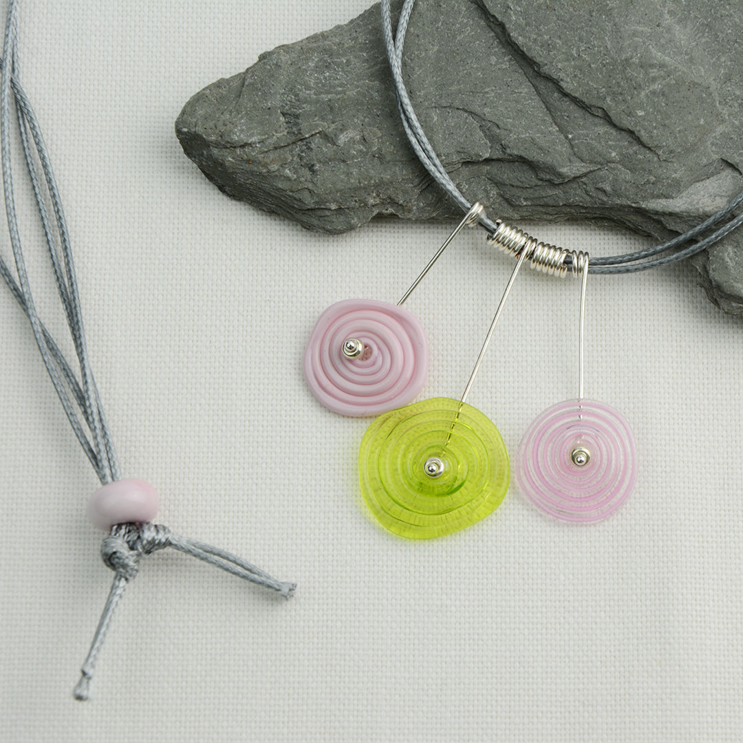 Three spiral beads in baby pink and lime green on silver headpin drops with silver spiral spacers on grey necklace cord