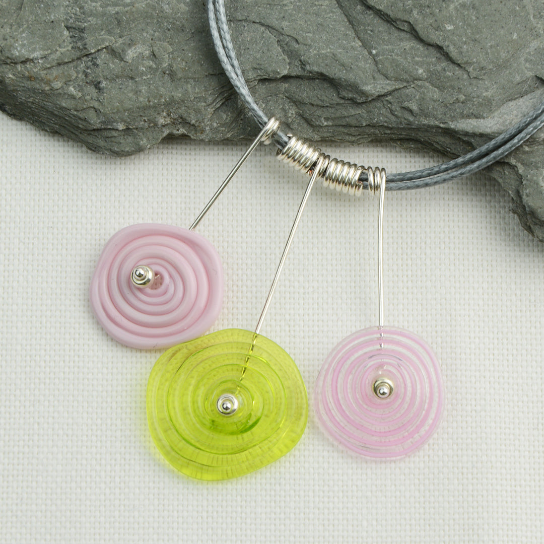 Three spiral beads in baby pink and lime green on silver headpin drops with silver spiral spacers on grey necklace cord