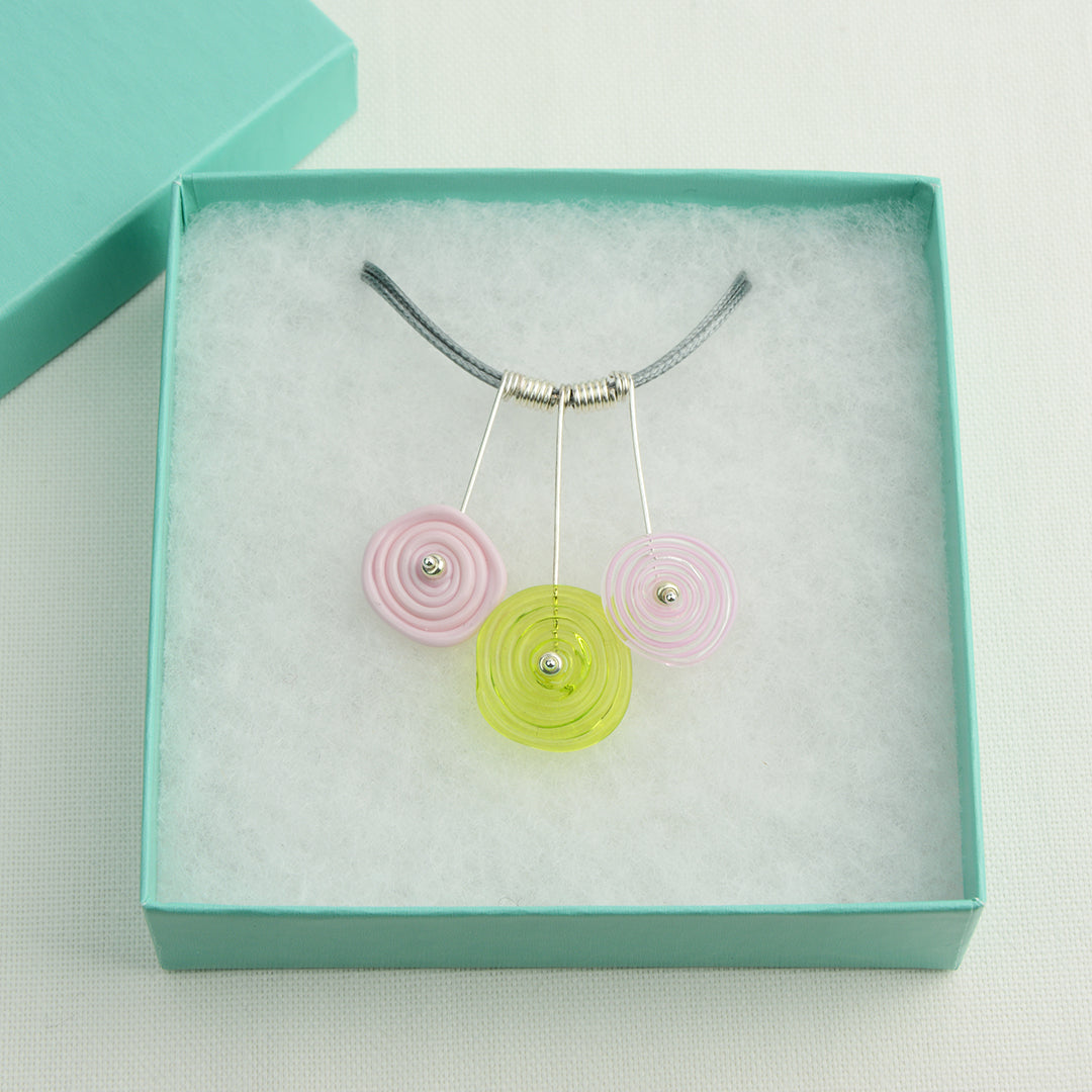 Three spiral beads in baby pink and lime green on silver headpin drops with silver spiral spacers on grey necklace cord in turquoise gift box