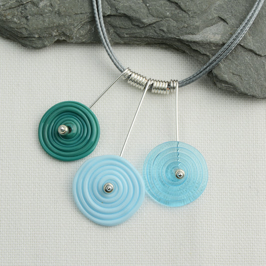 Three spiral beads in teal, pale blue and turquoise on silver headpin drops with silver spiral spacers on grey necklace cord