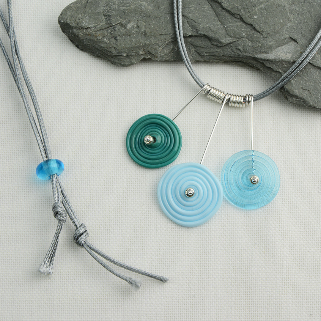 Three spiral beads in teal, pale blue and turquoise on silver headpin drops with silver spiral spacers on grey necklace cord