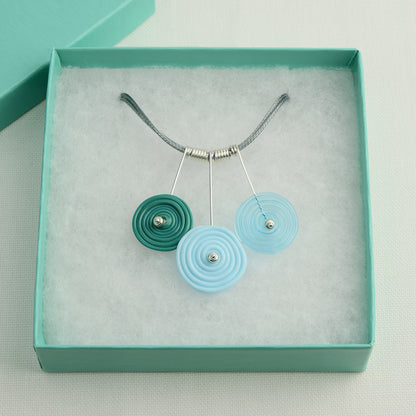Three spiral beads in teal, pale blue and turquoise on silver headpin drops with silver spiral spacers on grey necklace cord in turquoise gift box