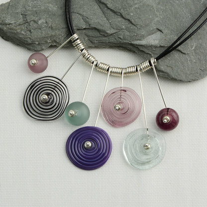 Four spiral beads and three spacer beads in shades of purple and grey on silver headpin drops with silver spiral spacers on black necklace cord