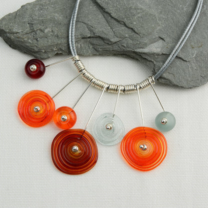 Four spiral beads and three spacer beads in bright orange, grey and red on silver headpin drops with silver spiral spacers on grey necklace cord