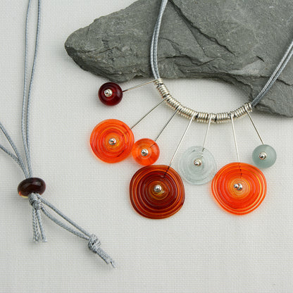 Four spiral beads and three spacer beads in bright orange, grey and red on silver headpin drops with silver spiral spacers on grey necklace cord