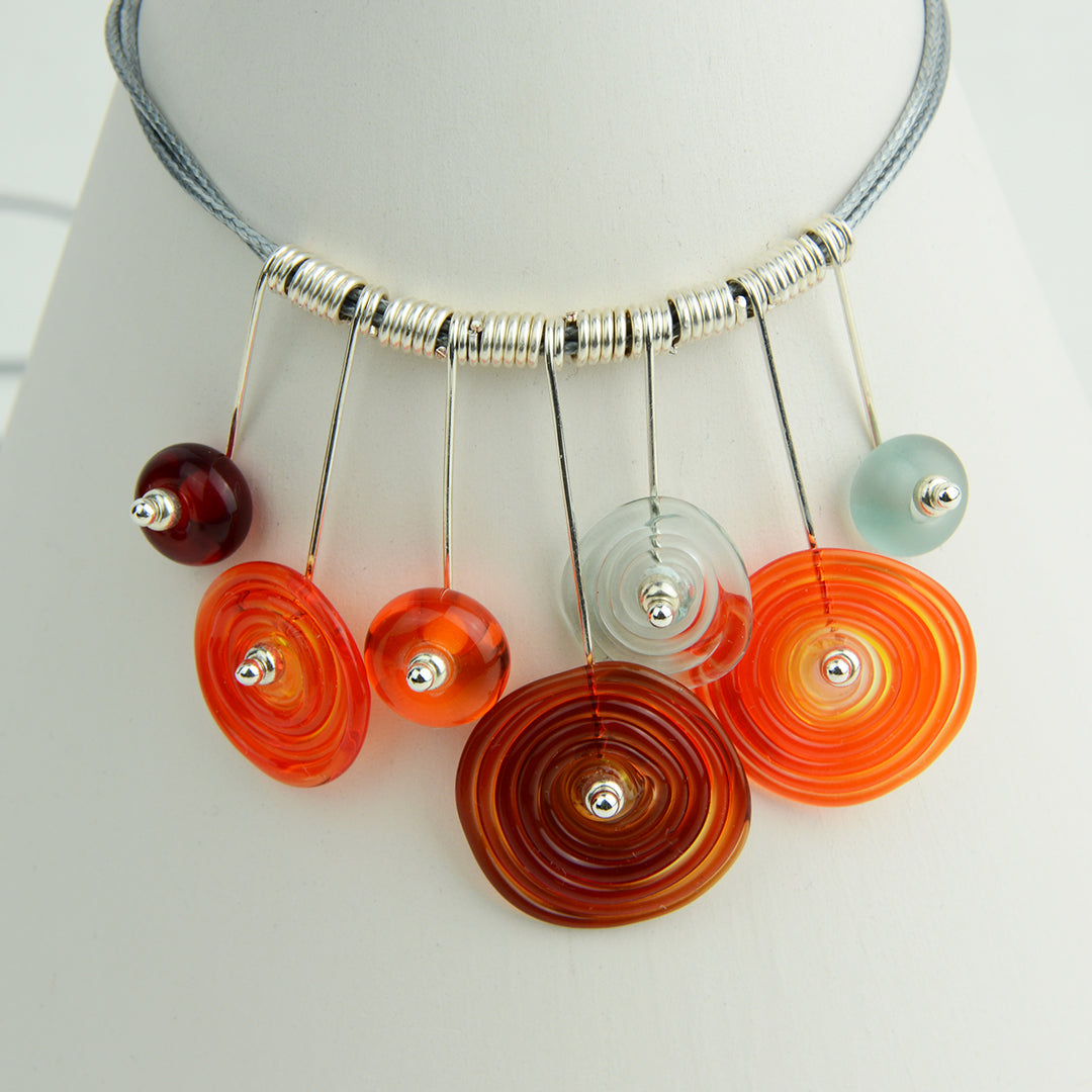 Four spiral beads and three spacer beads in bright orange, grey and red on silver headpin drops with silver spiral spacers on grey necklace cord