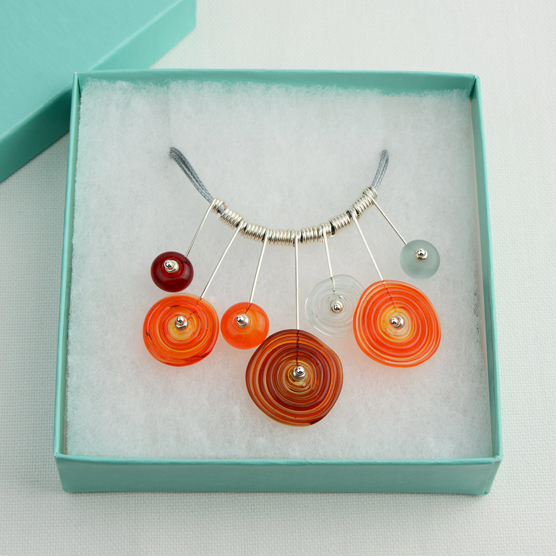 Four spiral beads and three spacer beads in bright orange, grey and red on silver headpin drops with silver spiral spacers on grey necklace cord in turquoise gift box