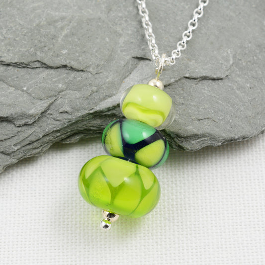 Two green glass beads and one green and blue bead making a pendant on silver chain